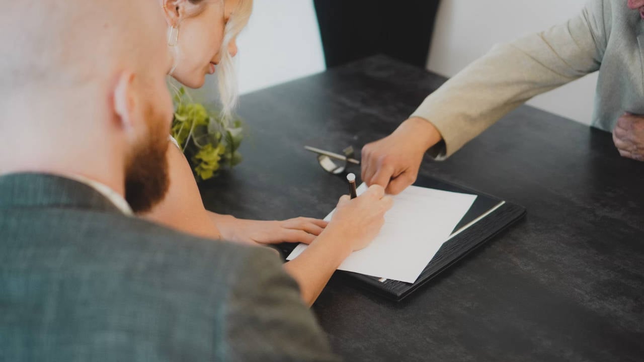 Tenant-Contract-Residential-Real-Estate A couple signing a contract with a professional in alight office with a dark wood table.