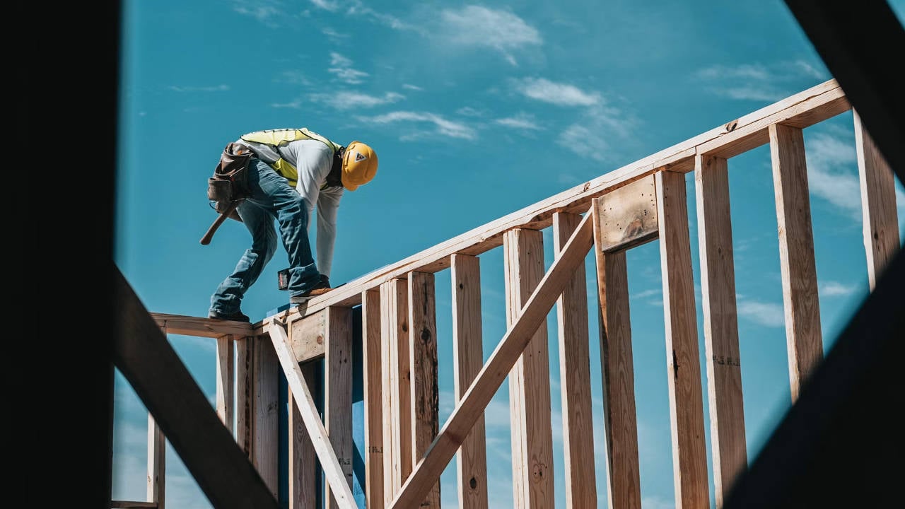 Construction-Worker-Framing-House Construction Worker Framing a House Against a Blue Sky
