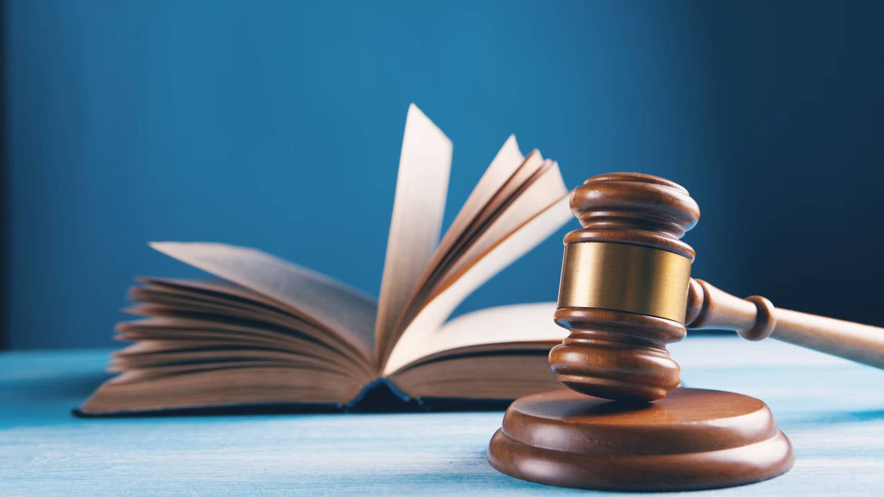Law-Book-And-Gavel A law book with pages turning against a blue background with a judge's gavel in the foreground resting on a podium.