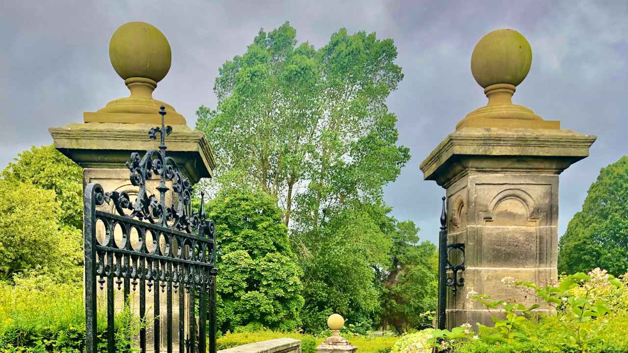 Gated-Community-With-Stone-Accent A metal gate with stone accents on the side and a wooded garden on the inside.