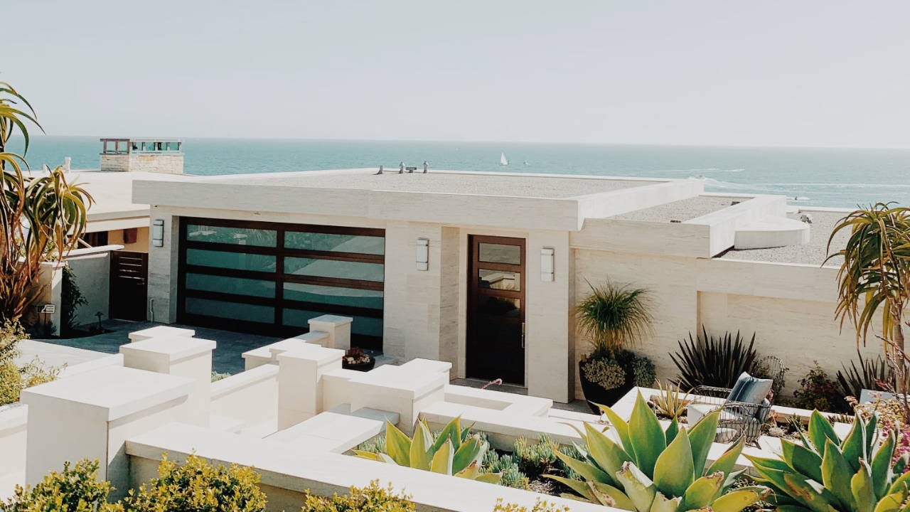 Modern white beach house with ocean in the background featuring concrete facade and glass garage.